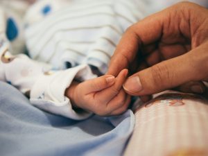 A parent's hand holding a baby's hand lying on the hospital bed.
