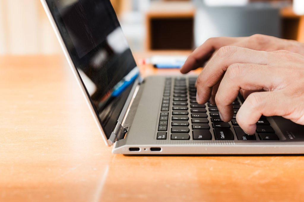 Fingers typing on a laptop atop a desk